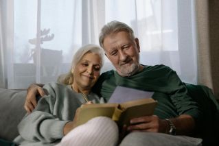 An elderly couple sharing a joyful moment while reading together at home.