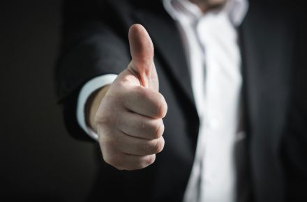 A close-up of a man's thumbs up gesture, symbolizing success and agreement.