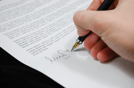 Close-up of a hand signing a legal document with a fountain pen, symbolizing signature and agreement.